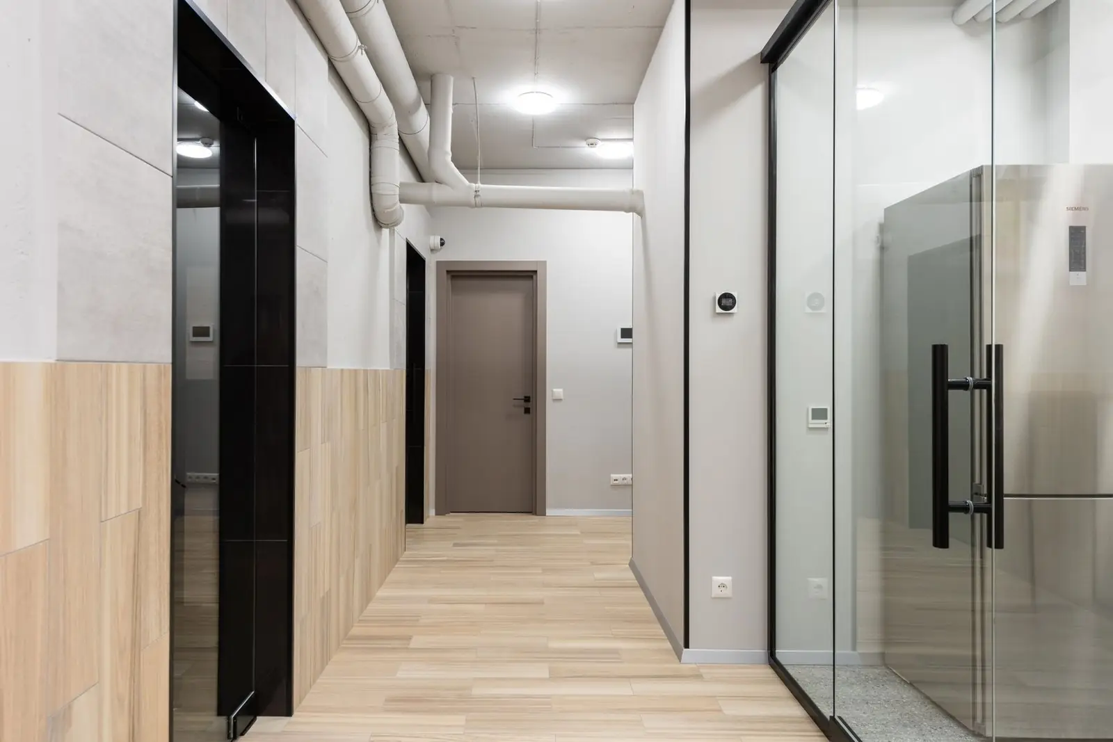 A bright office corridor with glass doors and a wood panelled wall
