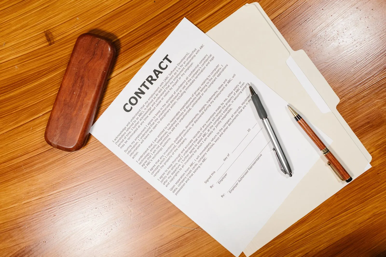 A printed contract with two pens on a wooden desk