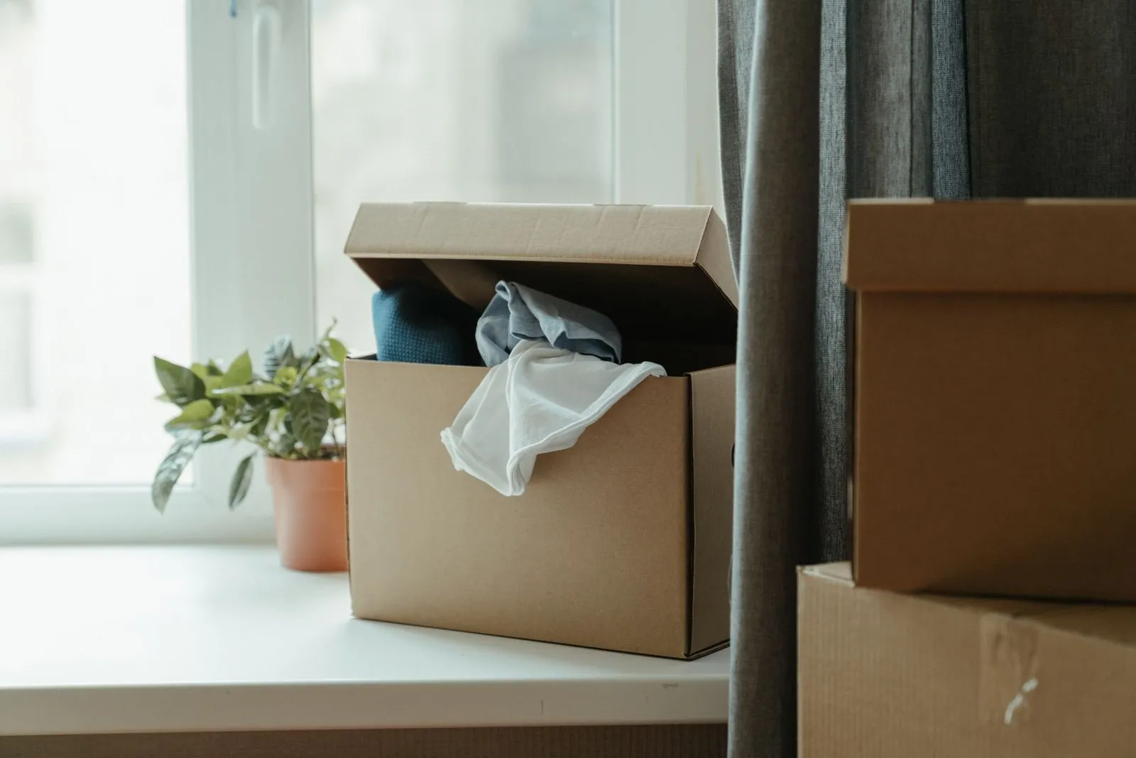Packed cardboard boxes beside a window in an empty flat