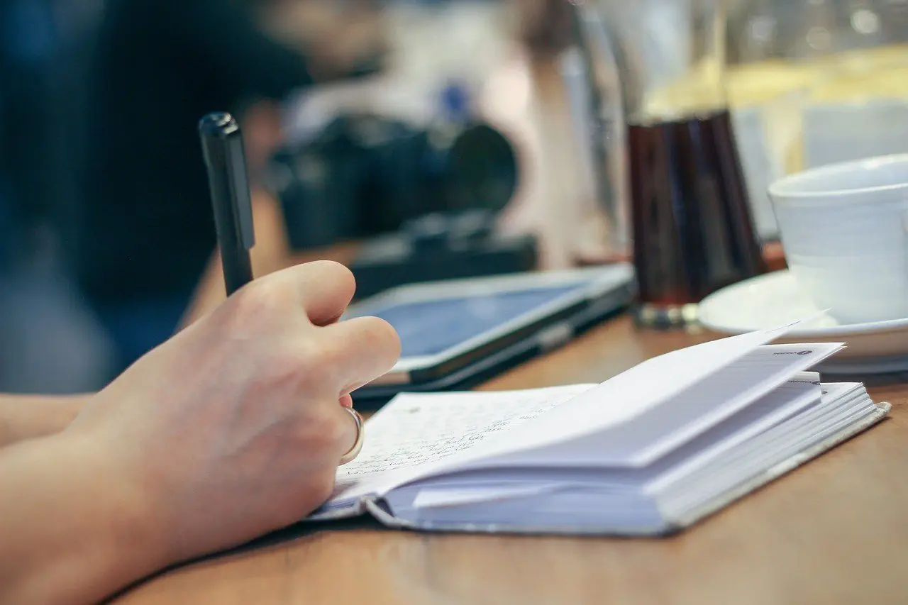 Hand writing in a notebook at a table