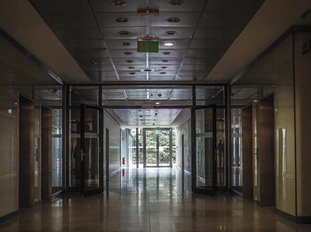 A long office corridor with glass doors and lifts on both sides