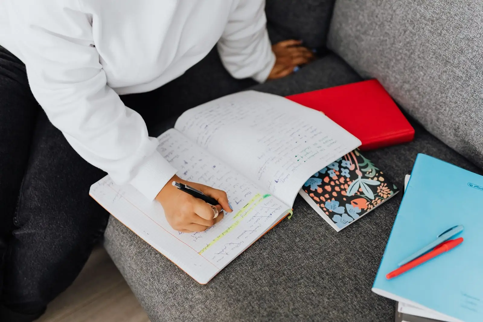 Person writing notes in a notebook on a sofa