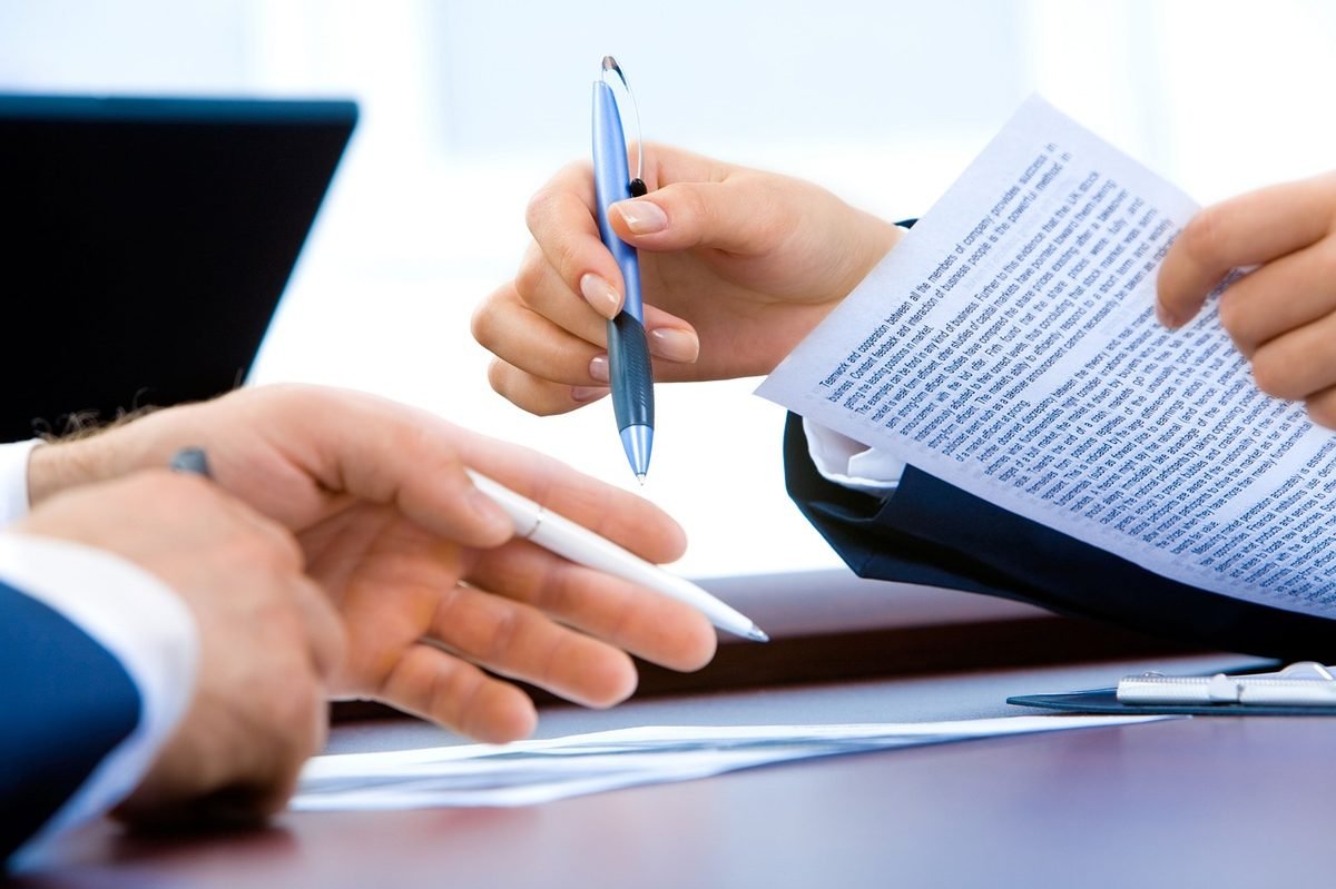 Two people reviewing and signing a contract with pens at a desk